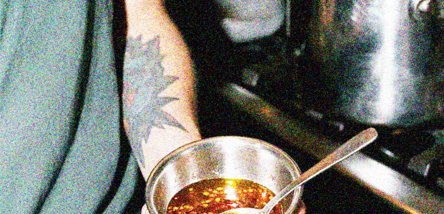 Chef holding a small bowl of oil in a professional kitchen.