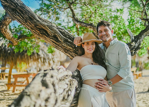 Pareja embarazada mirando a la camara junto a una rama de arbol en Playa Macao durante una sesion de fotos de embarazo tipo babymoon en Punta Cana Republica Dominicana