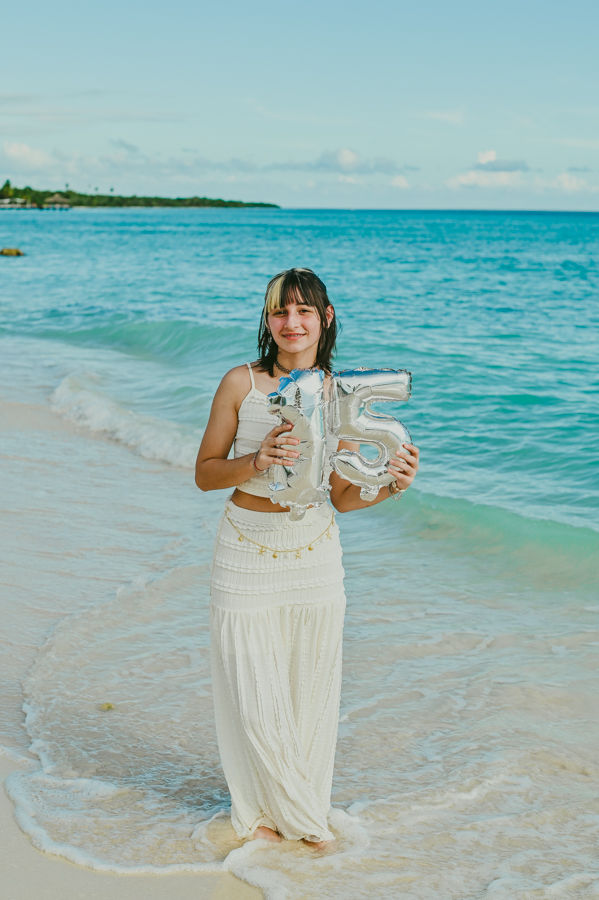 Quinceañera sonriendo con los globos del cumpleaños frente al mar Caribe.
