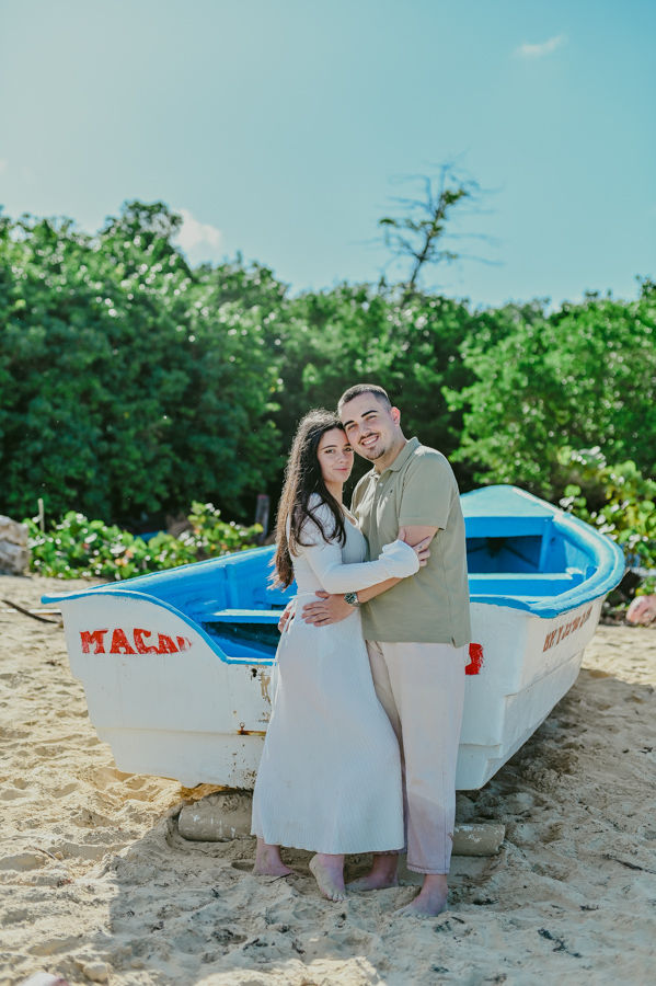 Pareja abrazandose frente a un barco de pescadores en la playa durante una sesion de fotos pre boda en Punta Cana realizada por un fotografo de boda en Punta Cana con estilo caribeno autentico.