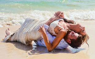 Pareja de recien casados riendo y rodando en la arena durante una sesion trash the dress en la playa en Punta Cana Republica Dominicana