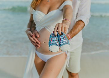 Expecting couple showing baby shoes during a maternity photoshoot on the beach in Punta Cana.