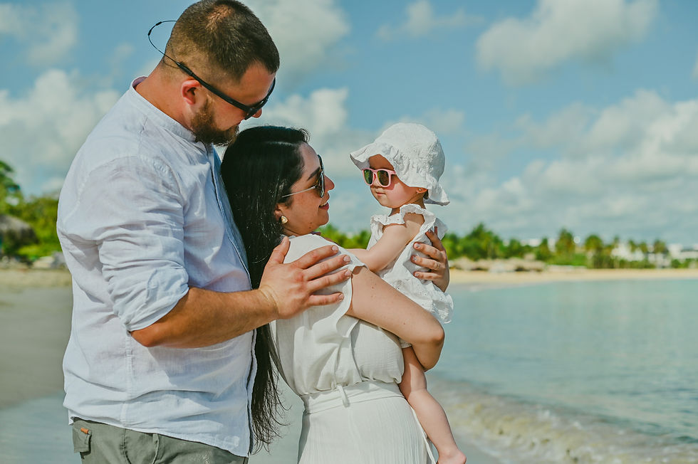Mamá sosteniendo a su bebé con sombrero y lentes de sol mientras papá se acerca a ellas en Playa Macao.