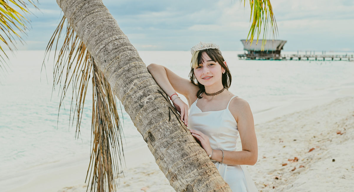 Quinceañera con corona junto a una palmera durante su sesión de fotos de 15 años en la playa de Punta Cana.