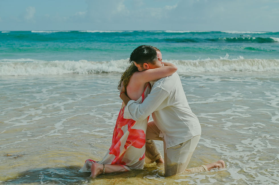 Diego and Javiera embracing on their knees at the shoreline of Uvero Alto Beach in Punta Cana Dominican Republic after a surprise marriage proposal, sharing an emotional and joyful moment by the Caribbean Sea near Excellence Punta Cana