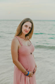 Mujer embarazada con vestido rosa mirando a la cámara durante su sesión en la playa frente al Hotel Impressive Punta Cana