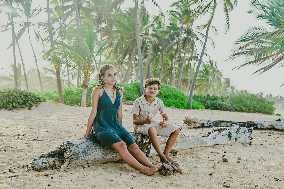 Brother and sister sitting on a driftwood log after their parents' vow renewal ceremony in Punta Cana, Dominican Republic