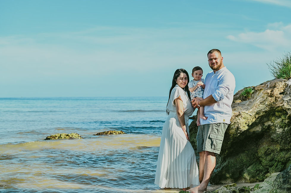 Mamá y papá con su bebé en brazos junto a una roca frente al mar de Playa Macao, Punta Cana.