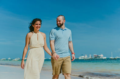 Couple walking hand-in-hand along the beach with a yacht in the background