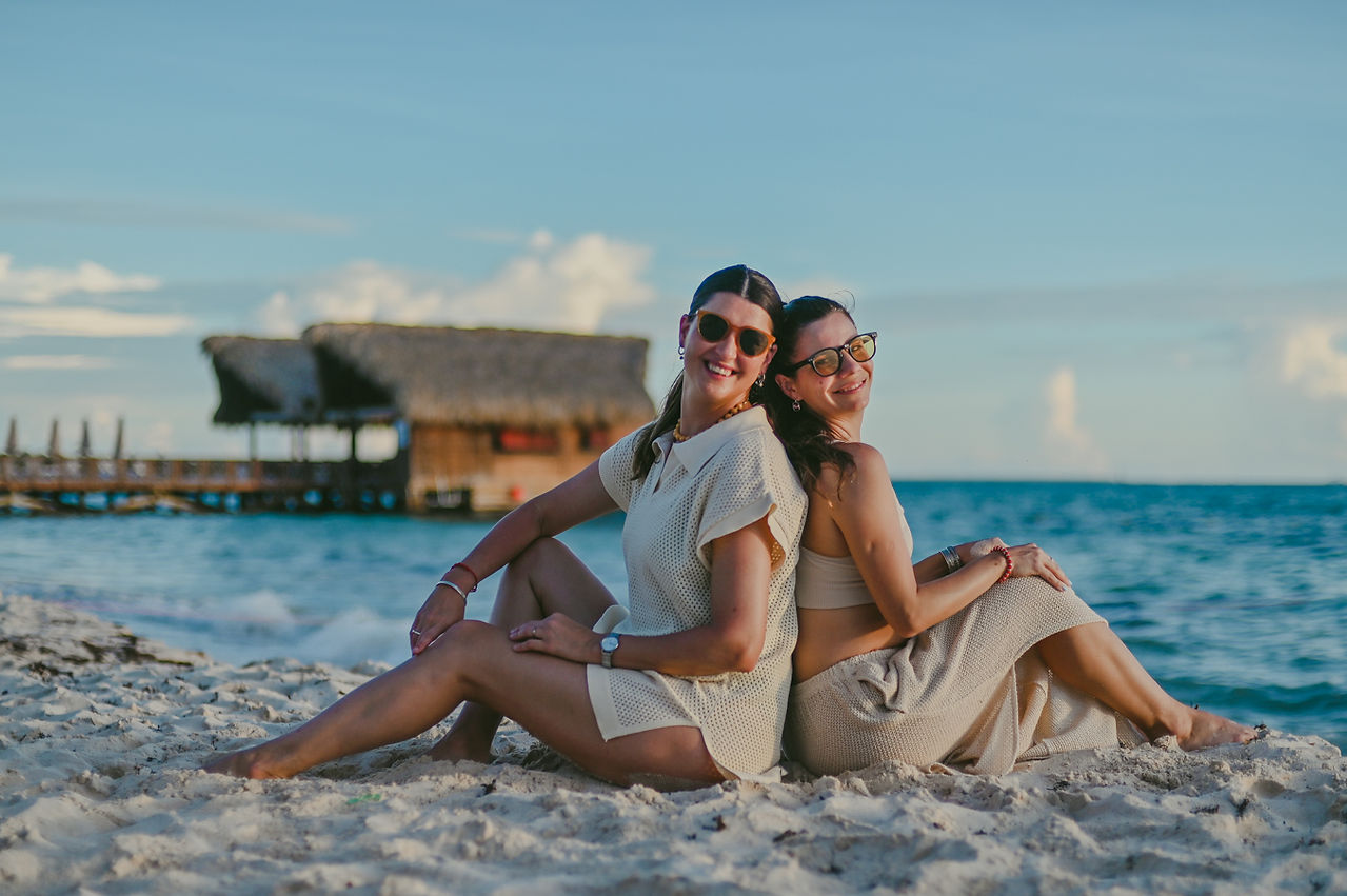 Majito y una amiga sentadas de espalda a espalda en la arena frente al mar