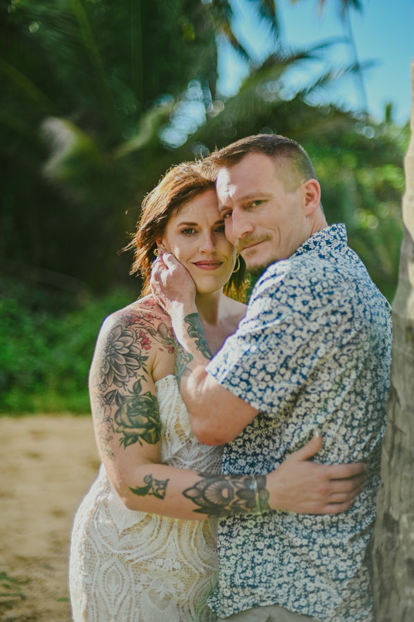 pareja tatuada abrazados mirando a la camara junto a palmera en playa Excellence Punta Cana