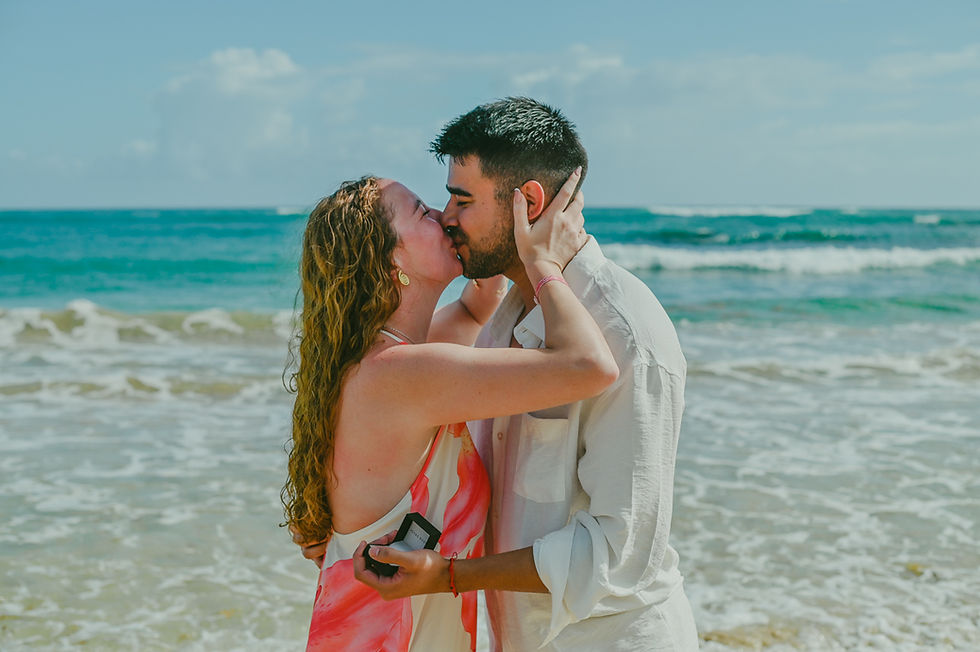 Diego and Javiera kissing on Uvero Alto Beach in Punta Cana Dominican Republic moments after their surprise marriage proposal, holding the engagement ring box in front of the Caribbean Sea during a romantic photoshoot photographed by Punta Cana Foto RD