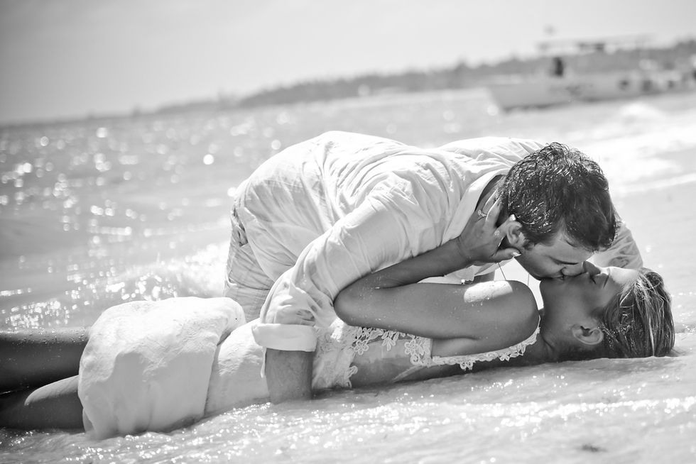 Recién casados besándose acostados en la arena en una fotografía en blanco y negro de una sesión trash the dress en Punta Cana