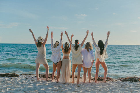friends raising their arms by the shoreline while looking toward the sunset