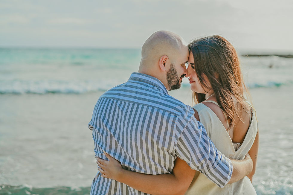 Pareja recién comprometida abrazándose frente al mar en una playa de Bayahibe durante una sesión de fotos de compromiso al atardecer.
