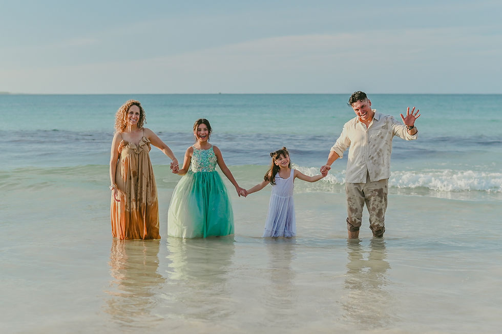 Family of four standing knee deep in the ocean while looking at the camera at Macao Beach during a family photoshoot in Punta Cana Dominican Republic