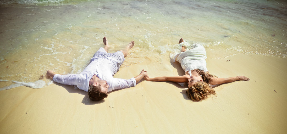 Fotógrafo en Punta Cana – sesión romántica de pareja acostados en la arena tomados de la mano durante una sesión de fotos de boda en la playa en República Dominicana