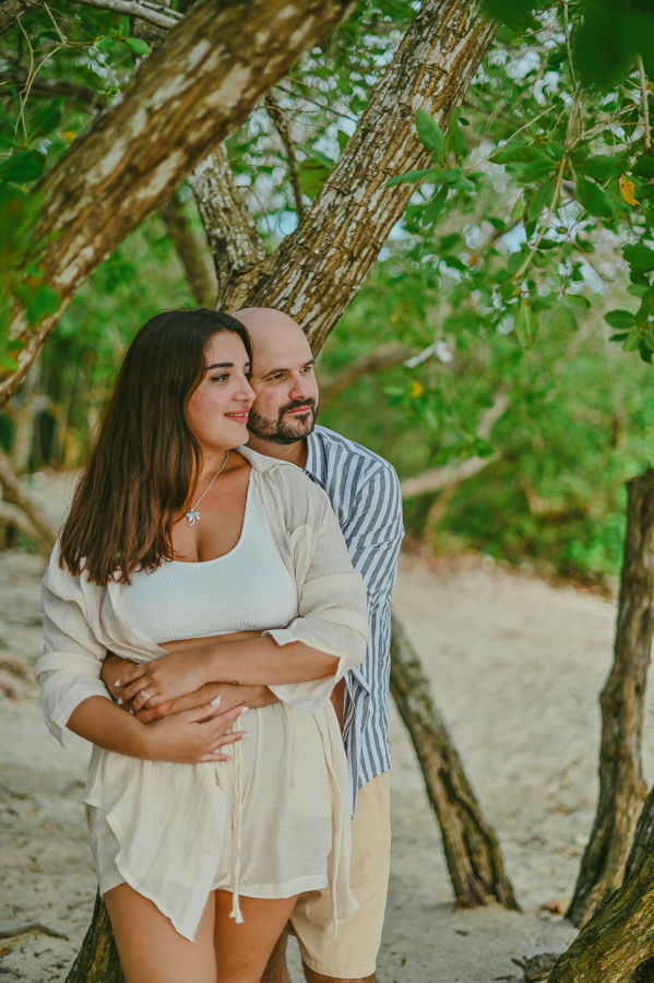 Pareja recién comprometida abrazándose en una playa de Bayahibe durante una sesión de fotos de compromiso rodeada de palmeras y el mar Caribe.