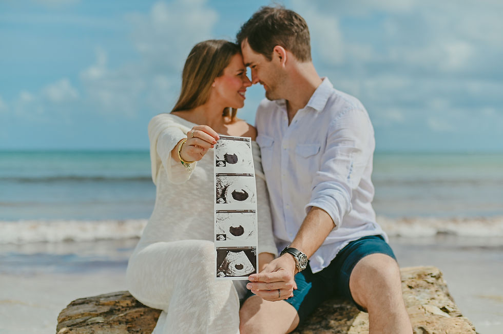 Foto artística de embarazo en Playa Macao, con la pareja sonriente y la ecografía en primer plano frente al mar Caribe.