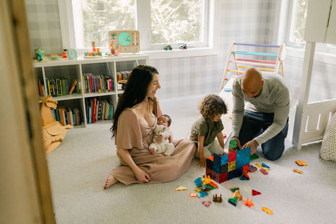 dad and son playing with magnet tiles while mom holds newborn baby