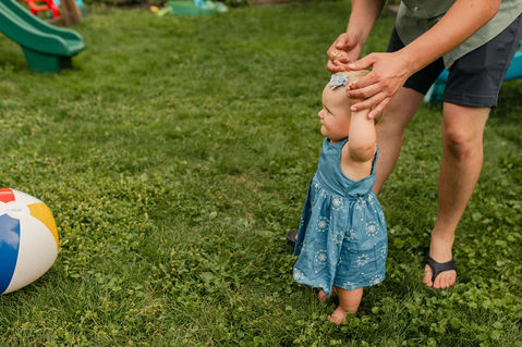 dad holding one year old baby's hands while she walks