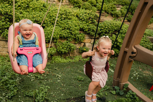 one year old baby and big sister swinging on backyard swingset