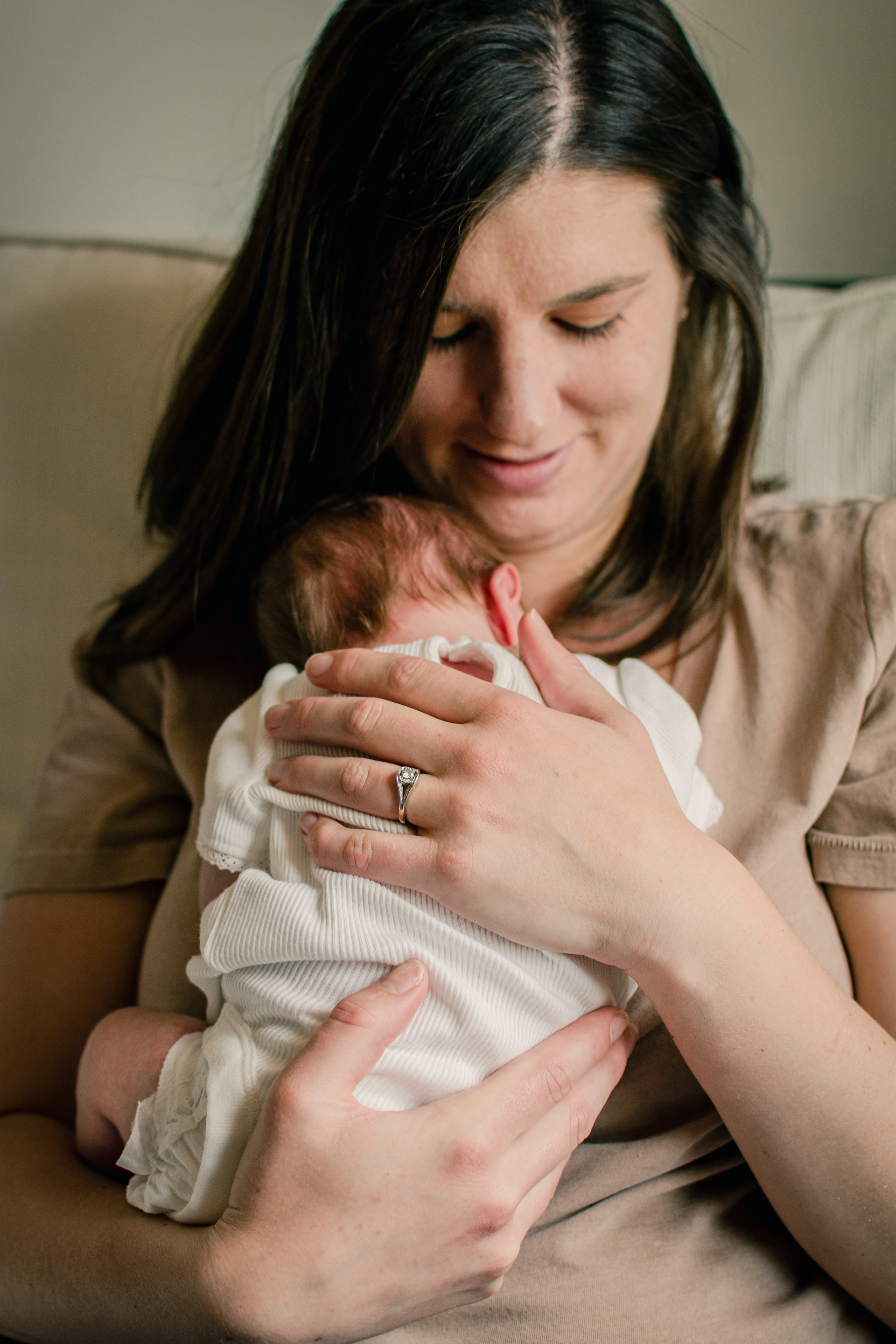 mom holding newborn in a white onesie against her chest