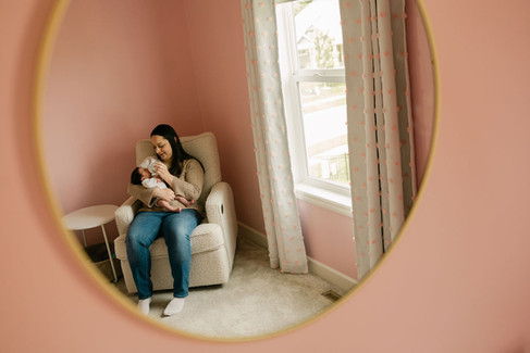 mom feeding newborn baby girl on a nursery chair
