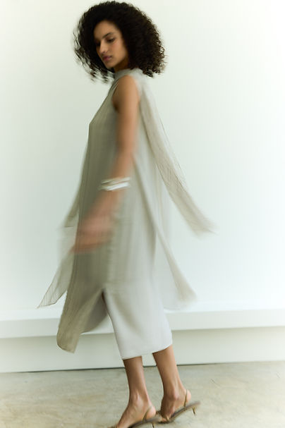 Second of three images of a model in motion wearing a parchment colour pinstriped silk georgette scarf dress. The photo is very blurred and shows the movement of the dress.