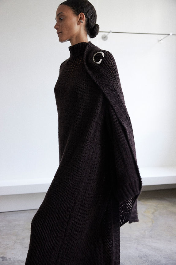 Model wearing oversized open knit poncho in tone 'Mahogany'. Poncho is closed with a rolled silver crescent brooch.