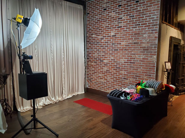Strike a Pose Picture Booth set up for a wedding at SODO Park by Urban Feast October 2022. Professional Camera Photo booth with external flash lighting and instant printing. Prop Table with black table cloth. This event used a brick wall in the venue as a backdrop.