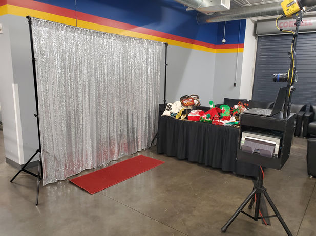 Strike a Pose Picture Booth set up at the LeMay American Car Museum for a photo booth at a company Christmas party. Professional Camera Photo booth with external flash lighting and instant printing. Silver sequence backdrop and holiday themed props.