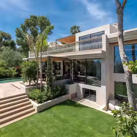 Luxury villa in Mallorca surrounded by lush greenery and a turquoise pool under a clear Mediterranean sky, showcasing elegant architecture and premium lifestyle investment appeal.