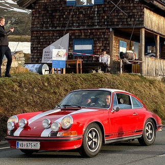 red Porsche 911 F-Model Coupe in front of wooden hut