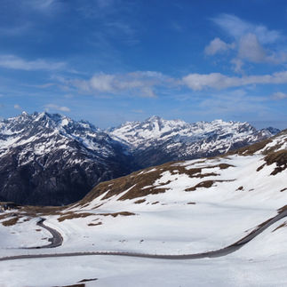 Helicopter view on curvy mountain road within snow-covered area with mountains in the back