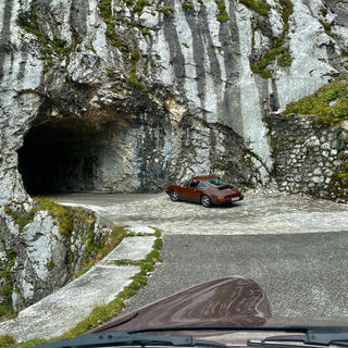 Porsche 911 cockneybrown entering handcrafted tunnel on mangart road