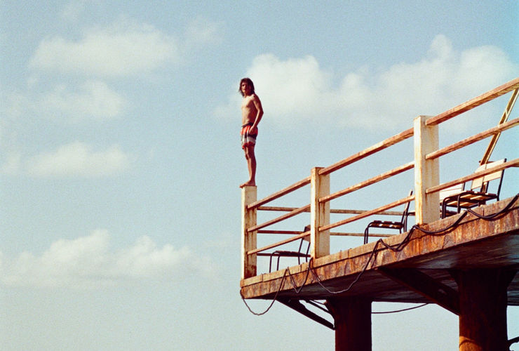 Une jeune fille atterrit avec concentration sur un tapis de gymnastique après avoir sauté d'une structure en bois, avec un arrière-plan flou d'autres équipements de parkour.