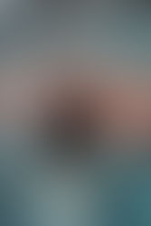 Jeune homme portant un bob marron brodé "ART" de la marque Aurum Tread, accroupi sur un sol urbain peint de motifs colorés bleu et orange. Il porte un sweat à capuche noir oversize, un jean clair et des sneakers blanches avec détails jaunes. Photo streetwear capturant l’esprit urbain et artistique de la collection Aurum Tread.