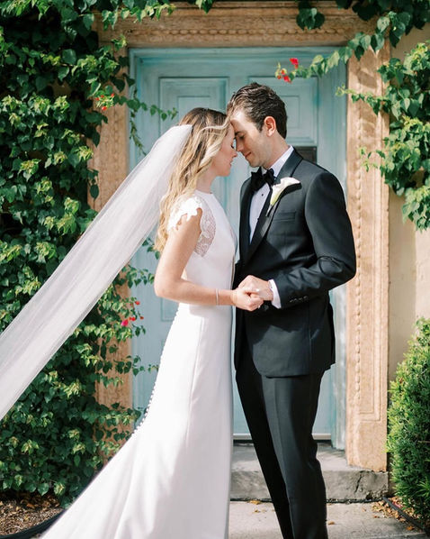 Bride and groom kiss in front of ivy-covered doors during Palm Beach wedding portraits.