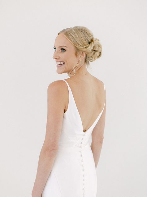 Bride looking over her shoulder showing open back of gown, low bun and veil visible.