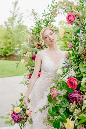 Bride framed by vibrant florals, featuring fresh and natural wedding day beauty styling.
