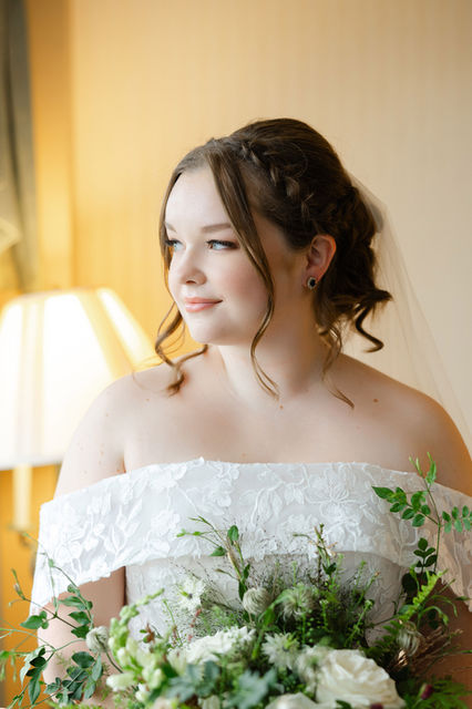 Bride looking off to the side in an off the shoulder wedding gown with natural bridal makeup and loose tendrils.
