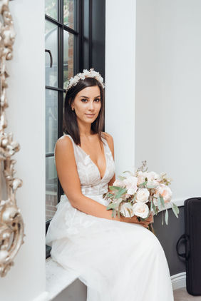 Photo by Monika Mistry Photography of a bride seated indoors holding her bouquet, wearing a fitted gown and tiara.