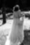 Bride walking through meadow in flowing wedding gown, black and white portrait.