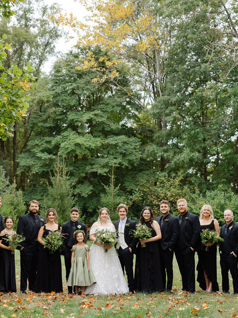 Wedding party standing together outdoors surrounded by greenery with cohesive hair and makeup styling.