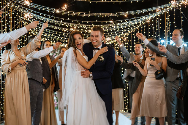 Bride and groom dancing beneath string lights as guests celebrate during a wedding reception.