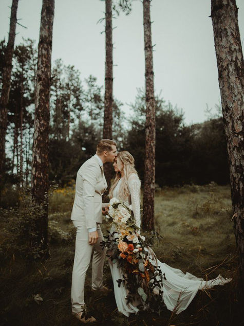 Bride and groom embracing outdoors in a forest setting with boho bridal hair and makeup by CampBride.