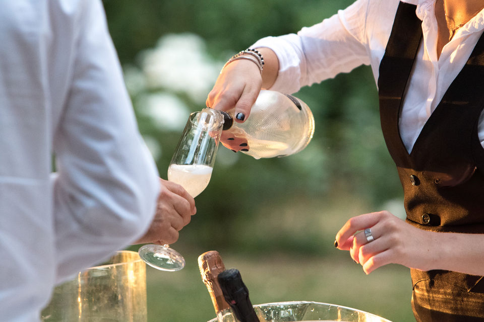 Bartender serving champagne outdoors during a wedding or private event.