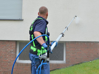 Ein Mann mit einer Teleskop-Sprühlanze spült Verschmutzungen von einer Fassade ab.