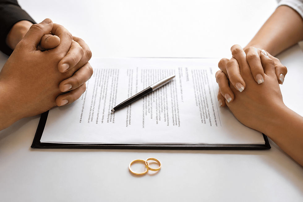Two people sitting across from each other with clasped hands over divorce papers and wedding rings on a table.